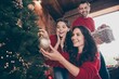 © deagreez - Family decorating Christmas tree together at home — mother and daughter hang a gold bauble while father brings a basket of ornaments, smiling and sharing joyful holiday moments