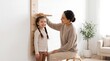© ZarVis - Happy Mother Measuring Cute Little Daughter Height with Wooden Growth Chart Ruler on Wall at Home