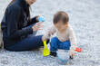 © leungchopan - Asian mother watching toddler son play with shovel and bucket outdoors