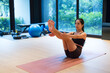 © leungchopan - Flexible woman performing boat yoga pose on mat in gym studio