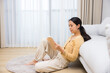 © leungchopan - Woman sitting on rug leaning against sofa in living room