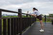 © leungchopan - Woman resting leg on wooden railing stretching in park 