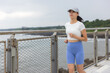 © leungchopan - Asian woman wearing cap jogging along ocean fence