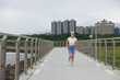 © leungchopan - Asian woman running forward on bridge path with city background