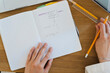 © Studio Marmellata - A person is writing marketing strategies and business goals in an open notebook on a wooden desk. They are using a yellow pencil to carefully plan their daily tasks.