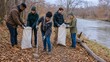 © AlenaSi - Group of volunteers cleaning riverside trail in late autumn with bags for collected debris. Participants are actively involved in environmental conservation efforts during fall season.