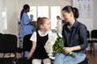 © DC Studio - Smiles, visitors and flowers with woman and girl sharing bright expressions beside a bouquet in hospital waiting area, for companionship, warmth, emotional support, kindness and hospital visitation.