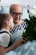 © DC Studio - Embrace, patient and flowers in hospital room as an older man holds a young visitor close beside a white bouquet, for affection, recovery support, comfort, companionship and emotional connection.