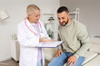 © Pixel-Shot - Healthcare consultation and medical advice, senior female doctor explaining diagnosis to young male patient in clinic office with clipboard and stethoscope