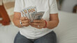 © Krakenimages.com - Woman holding and counting hundred dollar bills while seated on a bed in a building; financial security calm.