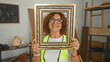 © Krakenimages.com - Woman carpenter smiling and holding an ornate picture frame with both hands in a woodworking studio among lumber and tools; craft pride.