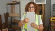 © Krakenimages.com - Woman carpenter in hi vis vest holds and inspects a rectangular wood panel with bare hands, turning and studying its edges in a workshop; concentration craft.