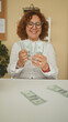 © Krakenimages.com - Woman counting dollar bills, hands visible at a desk in an office building; financial confidence contentment.