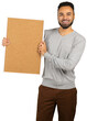 © fotofabrika - Man holding blank board in indoor setting, smiling at the camera, wearing gray sweater and brown pants