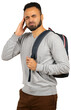 © fotofabrika - Man holding his head with a backpack on his shoulder stands with a pained expression indoors
