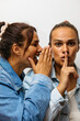 © Westend61 - Woman whispers a playful secret to her twin sister demanding silence