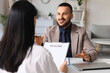 © Pixel-Shot - Job interview and recruitment process, smiling manager talking to a candidate holding a resume in a modern office during a professional hiring meeting