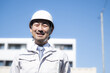 © kapinon - A smiling worker against the backdrop of an apartment building under a blue sky; imagery of property management, maintenance, renovation, and large-scale repairs; a middle-aged man