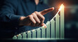 © MstZulakha - Man's finger pointing upward on a glowing green financial growth bar chart