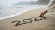 © ZAHEDA - Hand drawing the year 2024 in the sand on a beach with ocean waves in background