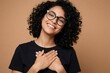© Viktor - Happy young afro woman with curly hair, glasses wears black t-shirt. Smiles brightly, places hands on chest, feels gratitude surprise. Portrait of joyful black female student expressing emotion