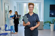 © Valerii Honcharuk - Smiling female doctor holding clipboard with stethoscope in hospital corridor