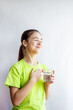 © Nataliia - Young girl in green shirt holding a glass of water with a grateful smile and hand on chest