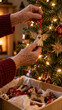 © Budi - Wrinkled hands hanging a worn wooden angel ornament by a red ribbon on a Christmas tree above a tissue-lined storage box, with warm lights showing gentle care for familiar holiday decorations