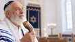 © Irina Kozel - Elderly Jewish man with white beard holds shofar inside synagogue, wearing tallit and kippah, blue ark curtain and candlelit backdrop