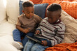 © Wavebreak Media - African American school-age boys sitting on cream sofa in living room, tapping black tablet sharing
