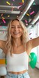 © Artsaba Family - A young Caucasian adult female smiles joyfully amidst falling confetti, wearing a white cropped top and light blue jeans