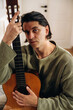 © standret - Pensive musician holding an acoustic guitar close to his face while seated indoors in soft natural light, vertical portrait of a male guitarist