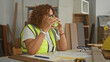 © Krakenimages.com - Woman carpenter sips coffee from a cup at a building woodworking table wearing high visibility vest and safety glasses; calm break.