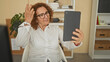 © Krakenimages.com - Woman touching tablet with finger while seated at desk wearing white shirt and glasses in office building; calm focus.