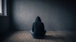 © Bano - Hacker sitting on wooden floor wearing dark hooded sweatshirt facing blank grey concrete wall inside empty room with window light casting soft shadows during daytime indoor scene
