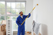 © Pixel-Shot - Home renovation and interior improvement, professional painter using a roller to paint a wall in a bright room during house refurbishment project