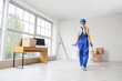 © Pixel-Shot - Home renovation and interior design, woman in workwear painting walls in new apartment with cardboard boxes and office desk in bright living room