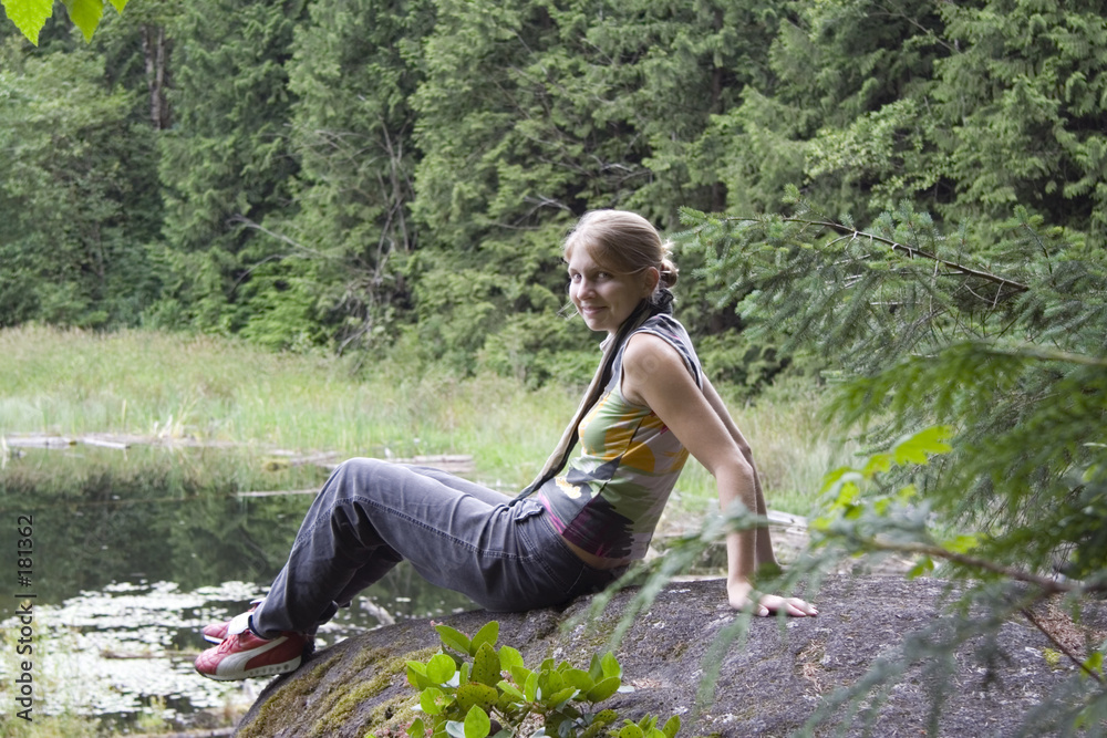 Εκτύπωση καμβά young woman climbing on a rock in front of fir trees and a tarn