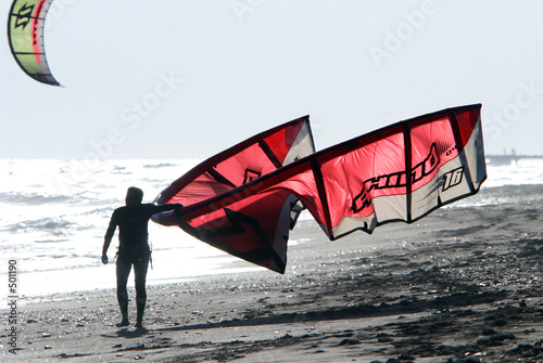 kitesurfer walking along the sandy beach at the end of a busy da