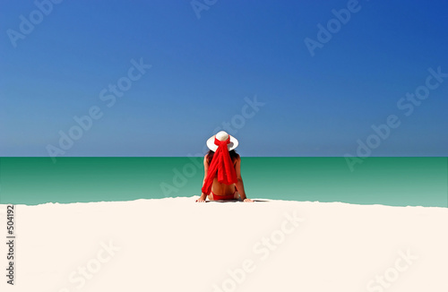 woman in red hat and bikini sitting all alone on empty beach