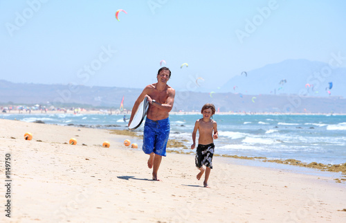 young father and son running along beach with surfboard