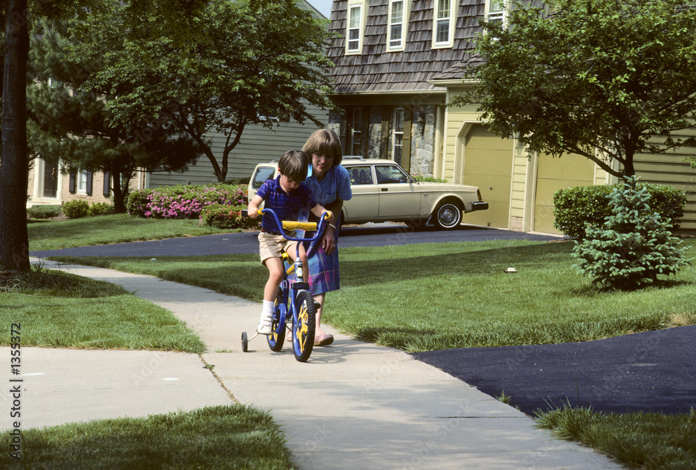 Fototapeta premium mother helps son learn to ride a bike