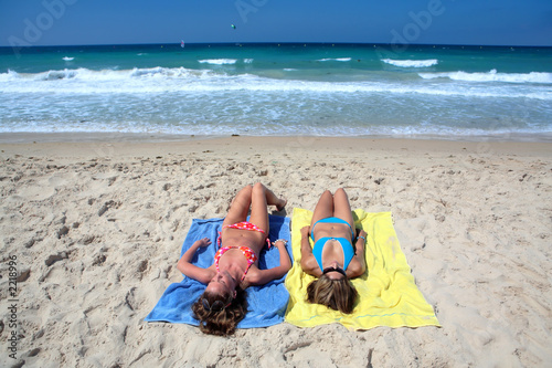 two sexy young girls laying on a sunny beach on va