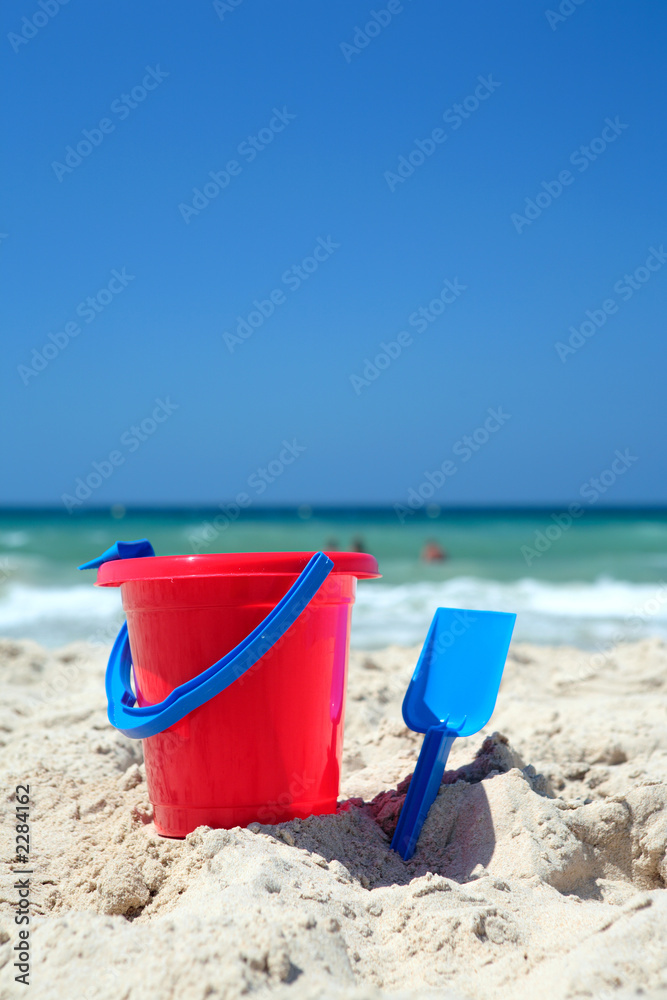 red bucket and blue spade on sunny, sandy beach red bucket and blue spade on sunny, sandy beach