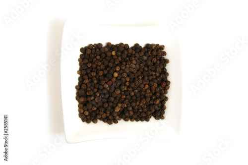 whole black pepper in square white bowl isolated