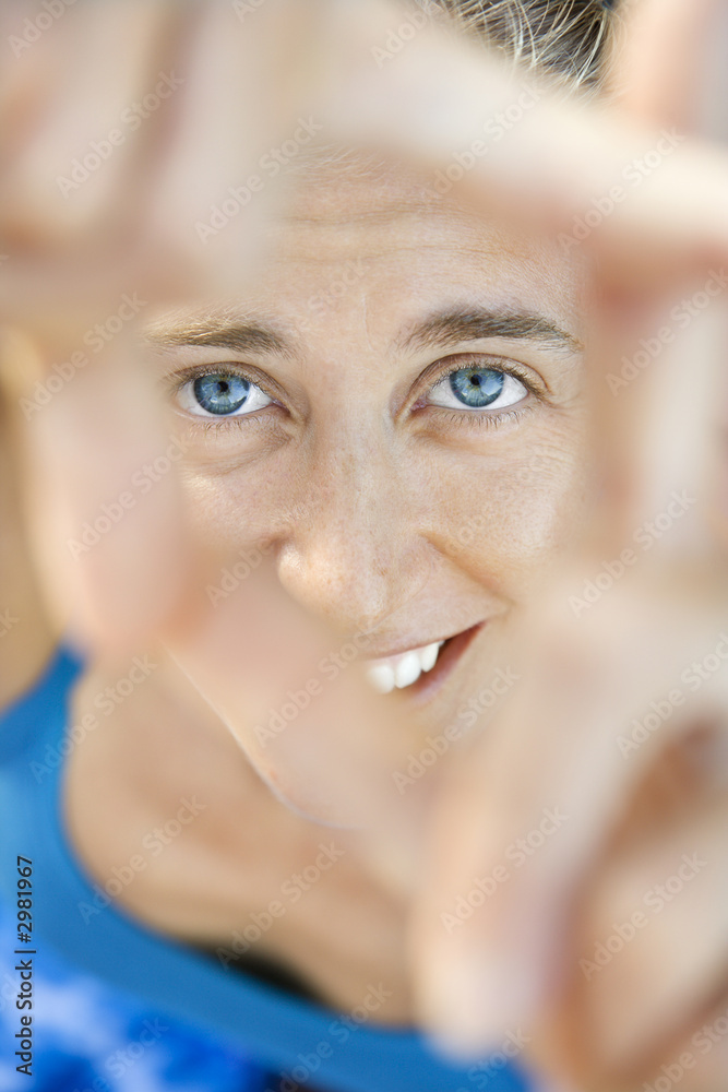 Close-up of woman smiling through framed fingers. Close-up of woman smiling through framed fingers.