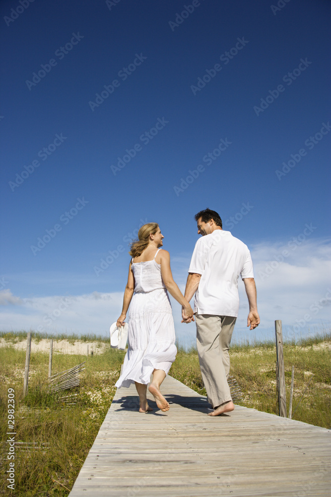 Couple holding hands walking down path.