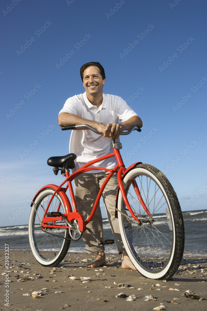 Mid-adult man leaning on red bike at beach. Mid-adult man leaning on red bike at beach.