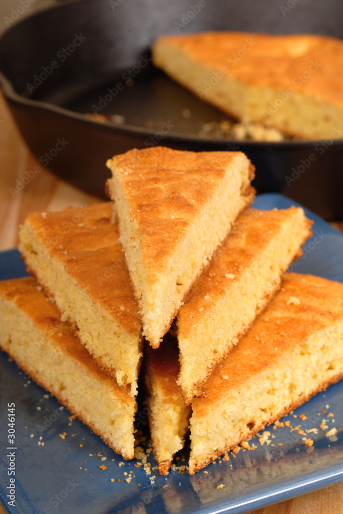 stack of cornbread on blue plate with black skillet in backgroun