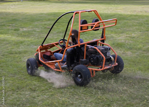 Go-kart drive by with dusty flying behind on the grassy field